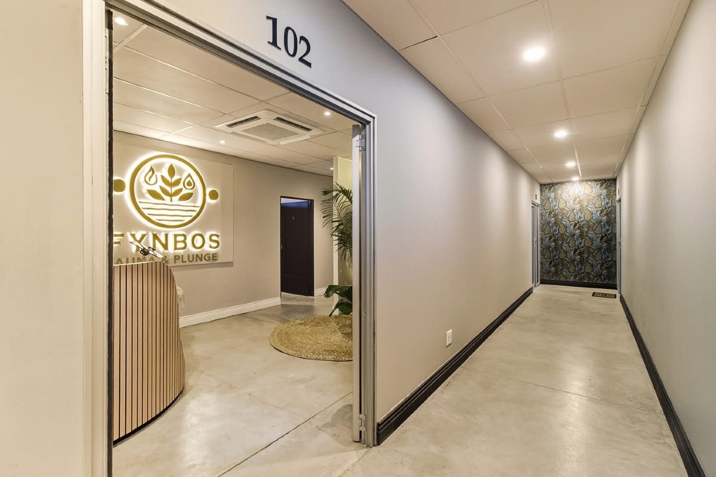 Reception at Fynbos Sauna & Plunge with illuminated logo sign, slatted timber counter and polished concrete floor